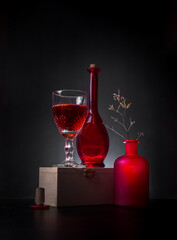 Modern still life with red bottles and wine in a wine glass on a dark background
