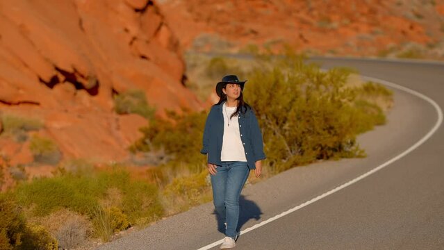 Young woman wearing a cowboy hat walking down a lonesome road in the desert of Arizona - travel photography