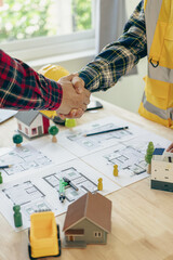 Yellow hard hat on table and house design print design with construction team handshake greeting start new project contract plan in office center at construction site partner and contractor