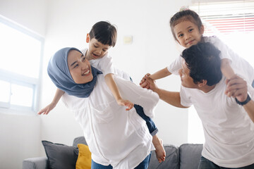 Obraz premium Cheerful Asian mom and dad piggy back their children in living room