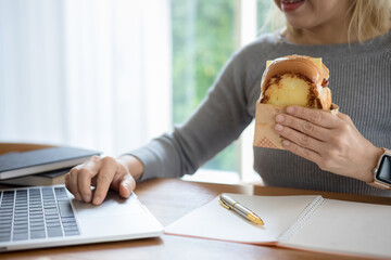 Student sitting in cafe, eating fast food and watching laptop