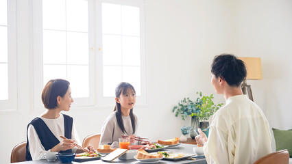 A family of an Asian girl and her parents sit around the dining table and enjoy a meal.