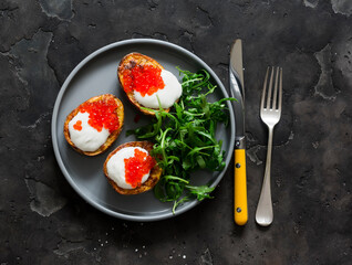Delicious tapas, appetizer - grilled potatoes with sour cream and red caviar and arugula salad on a dark background, top view