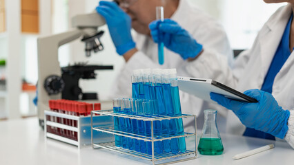 Two senior Asian men and women are scientists researching biology and chemistry. Couple wearing glasses and looking at microscope in laboratory with glass tubes on table