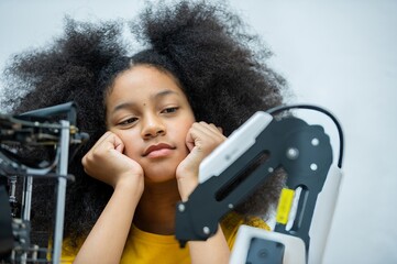 A young girl is looking at a robotic arm.