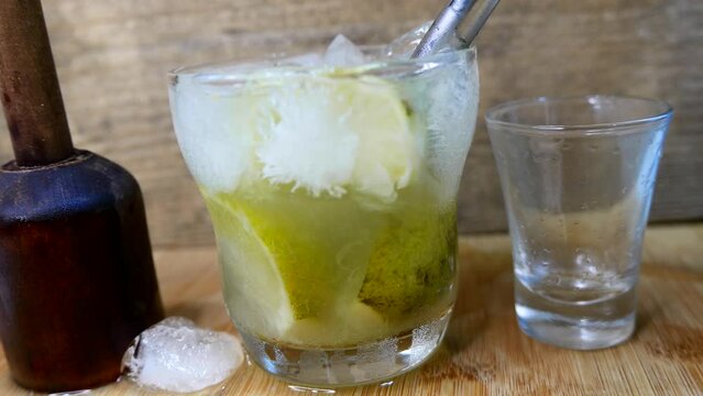 Putting a straw in a caipirinha glass. Caipirinha drink recipe, close-up shot: sugarcane liquor, sugar, ice, and lemon. Drinking caipirinha. Making drinks. Inserting a metal straw into a caipirinha. 