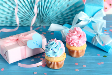 Delicious cupcakes with question mark, gift boxes and decorations on blue wooden table against...