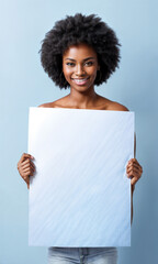 A young woman with a vibrant smile and a curly afro hairstyle stands holding a blank white sign in front of her.