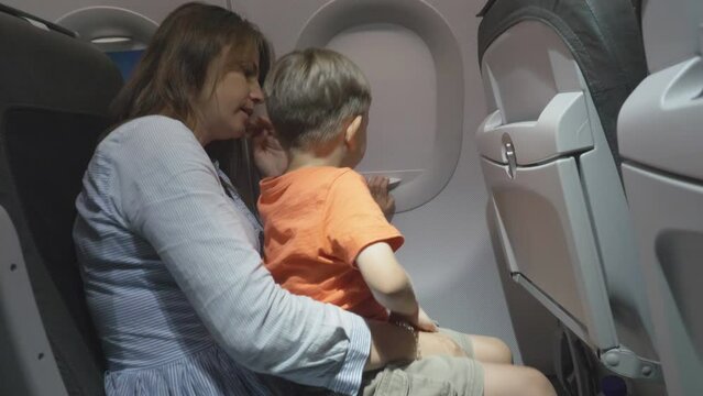 Restless little boy in mother's lap on airplane night flight