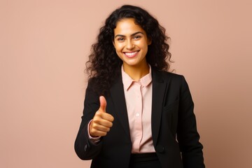 Confident South American businesswoman in her mid-30s, against a soft beige background, smiling warmly and giving a thumbs-up sign.
