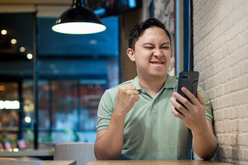 Asian man Engaging with Smartphone in a Modern Cafe Setting. Looking to good news on his phone...