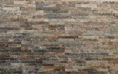 External stone wall made of rock panels with long horizontal bricks. Colors are brown, gray and...