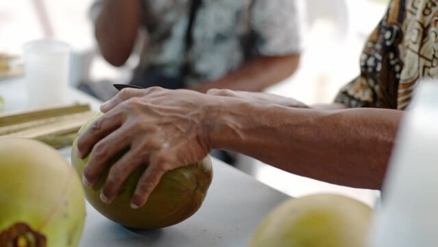 Man making art carving on green coconut with small knife, cutting closeup