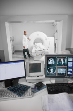 Medical computed tomography or MRI scanner. Doctor making MRI, patient lying on couch. Male specialist wearing white robe and glasses, looking at camera, smiling. Concept of modern diagnostics.