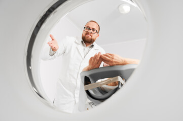 Medical computed tomography or MRI scanner. Male radiologist examine female patient, looking to the...