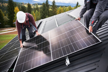 Builders building photovoltaic solar module station on roof of house. Men electricians in helmets...
