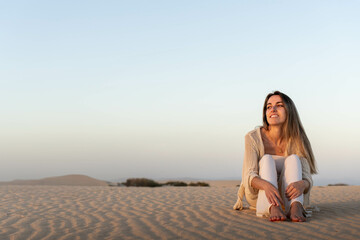 Fototapeta na wymiar Happy young woman sitting on sandy dunes