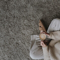 Woman sitting on fluffy carpet with cup of coffee. Cozy morning routine
