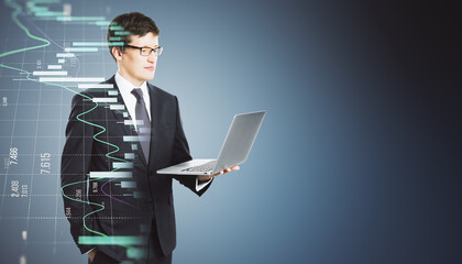 Side view of young european businessman using laptop with growing blue forex chart hologram on...