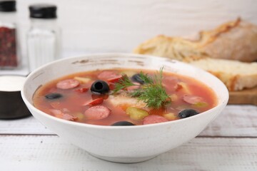 Meat solyanka soup with thin dry smoked sausages in bowl on white wooden table, closeup