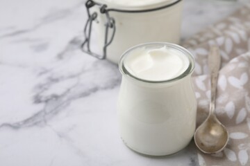 Delicious natural yogurt in glass jar and spoon on white marble table, closeup. Space for text