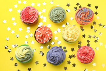 Delicious cupcake with bright cream and shiny confetti on yellow background, flat lay