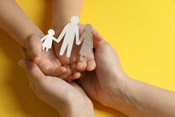 Mother and child holding paper cutout of family on yellow background, closeup