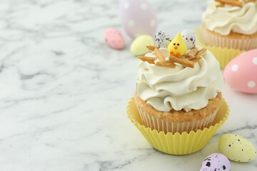 Tasty Easter cupcake with vanilla cream and candies on white marble table, space for text