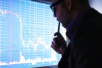A businessman is looking at a graph on a monitor. An exchange broker evaluates stock market trends. A man with glasses in front of a curve of the dynamics of the economy. - obrazy, fototapety, plakaty