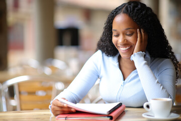 Happy black student memorizing notes in a coffee shop