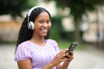 Happy black woman looks at you with phone and headphone