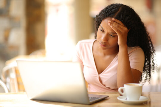 Worried black woman checking laptop content in a bar - Powered by Adobe