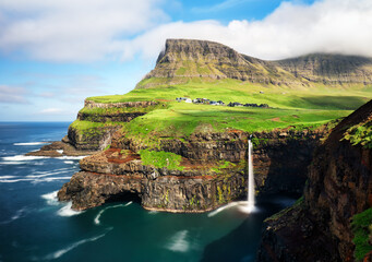 Faroe Islands waterfall Múlafossur near village Gasadalurron the Island Vágar. Green mountain caost landscape.
