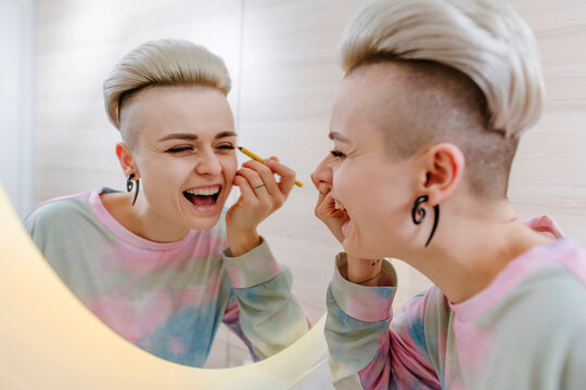 Happy young woman applying mascara looking in mirror at home