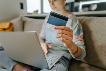 Woman showing credit card sitting with laptop on sofa at home