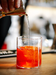 Bartender making Negroni cocktail on bar counter. Negroni classic cocktail and gin short drink with...