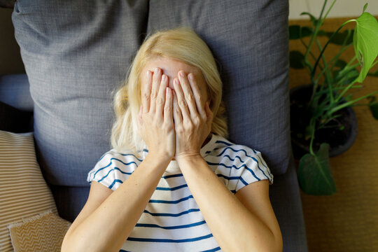 Mature woman covering face with hands at home - Powered by Adobe