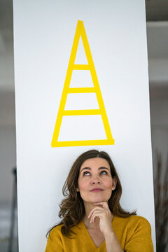 Thoughtful creative businesswoman looking at pyramid sign on wall