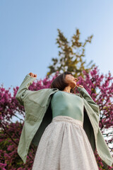 Fototapeta premium portrait of a happy girl. urban style and fashion. A young brunette smiles happily while walking in a city garden. Young stylish girl in a shirt.