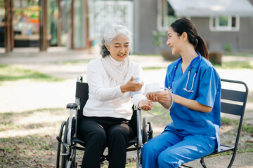 Elderly asian senior woman on wheelchair with Asian careful caregiver and encourage patient, walking in garden. with care from a caregiver