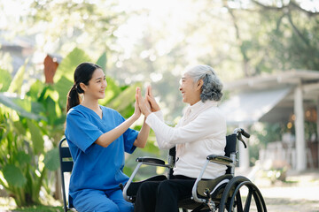 Fototapeta na wymiar Elderly asian senior woman on wheelchair with Asian careful caregiver and encourage patient, walking in garden. with care from a caregiver
