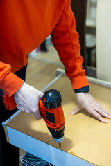 carpenClose up of a woman using cordless screwdriver for assembling furniture at home. Independent woman repairing furniture at home.ter working on a saw