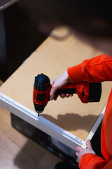 Close up of woman hands assembling furniture from chipboard, using a cordless screwdriver. 