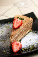 layer sponge cake with strawberries on a black plate on wooden background