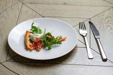 piece of pizza with smoked salmon and arugula on a white plate
