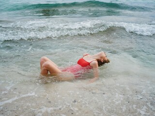 Woman lying on the ocean on the beach in the waves in a red swimsuit, a hotel vacation