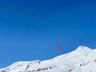 A red seat of skiing lift in the mountains on a blue sky background