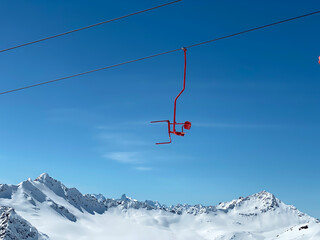 A red seat of skiing lift in the mountains on a blue sky background