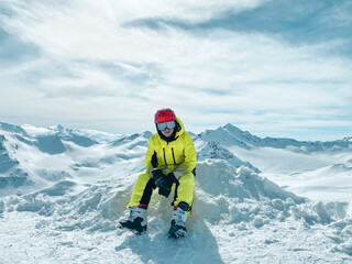 A teenager in a bright sport skiing suit sitting on the snow in the mountains