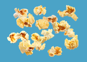 Tasty fresh popcorn flying on light blue background